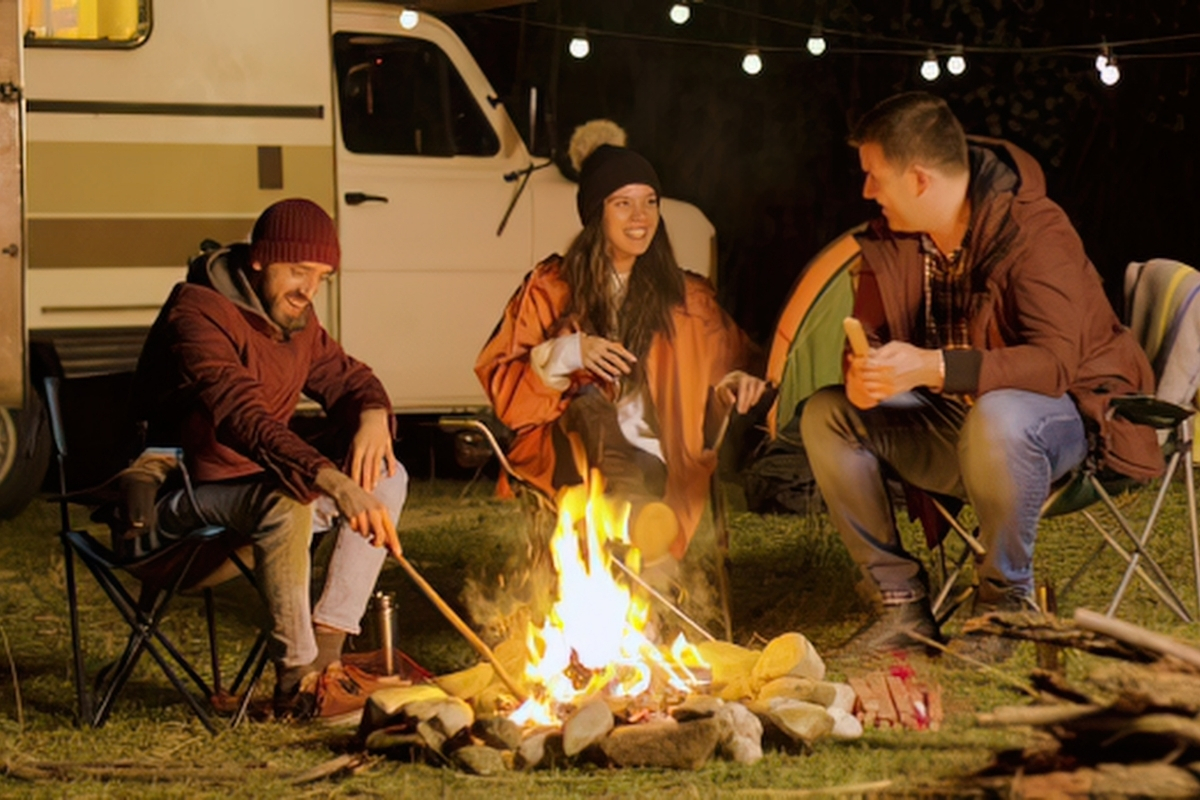 Trois personnes autour d'un feu de camp devant un van